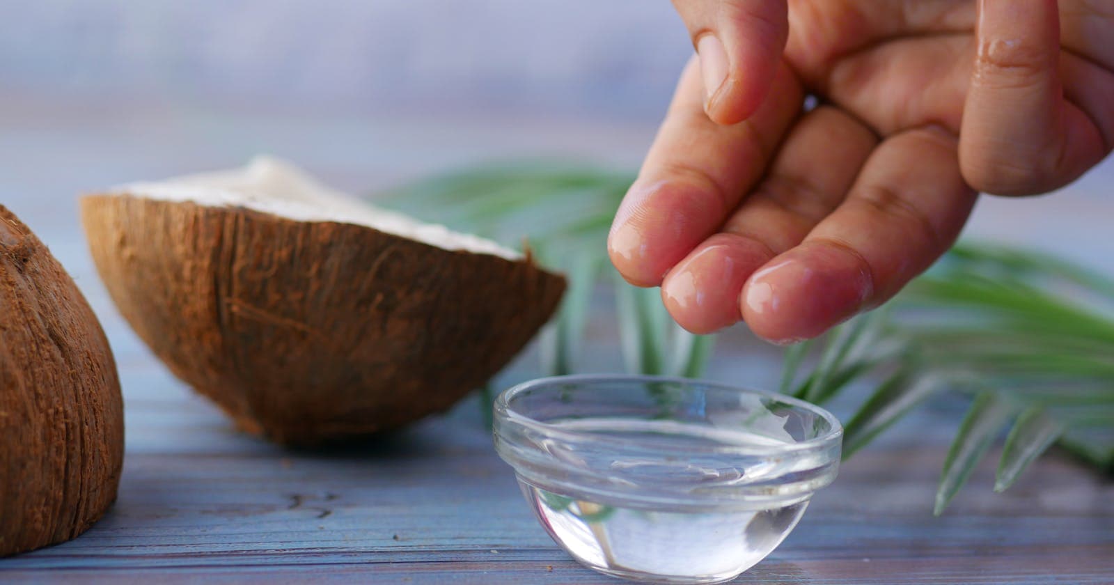 Hands dipping into coconut oil beside fresh coconut halves — the morning oil-pull ritual