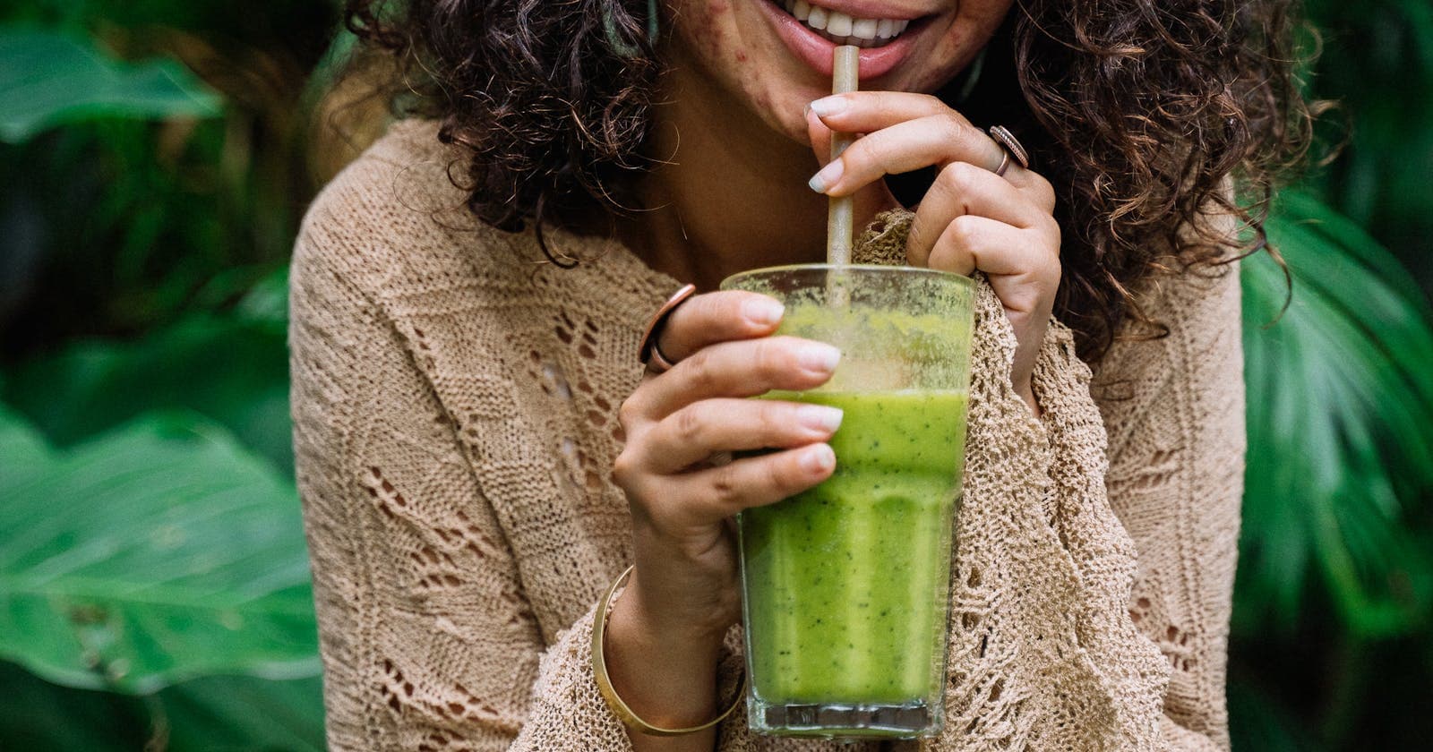 Young woman with curly hair enjoying a green smoothie in a garden, Ayurveda's friendly approach to weight